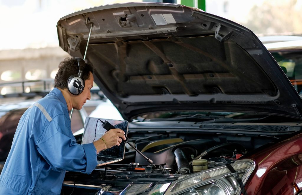 Asian automotive mechanic with blue uniform use electronic tools to check the car